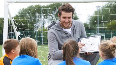 entraîneur qui parle à des jeunes à coté d'une cage de football